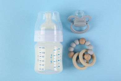 Photo of Feeding bottle with milk, teether and pacifier on light blue background, flat lay