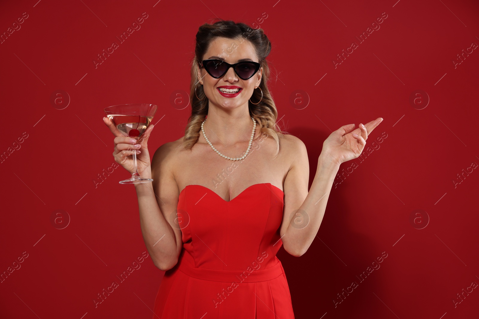 Photo of Happy woman with cocktail on red background. Pin-up vibe portrait