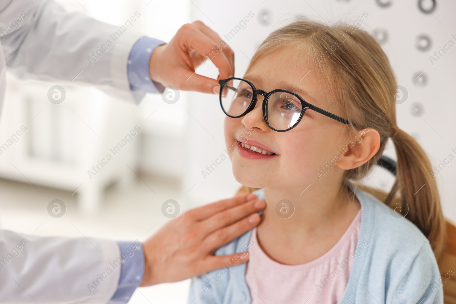 Photo of Vision testing. Ophthalmologist giving glasses to little girl indoors, closeup