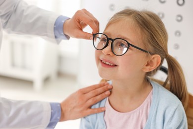 Vision testing. Ophthalmologist giving glasses to little girl indoors, closeup