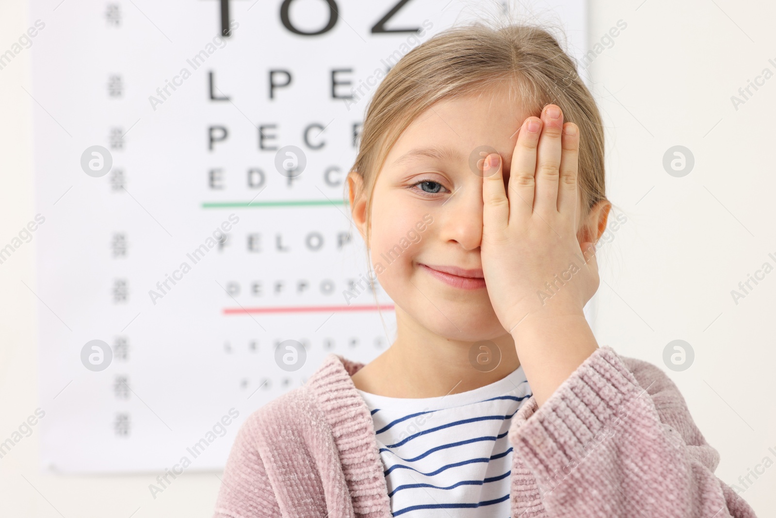 Photo of Little girl covering her eye against vision test chart