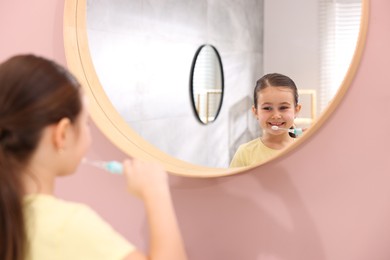 Photo of Cute girl brushing her teeth near mirror in bathroom, selective focus