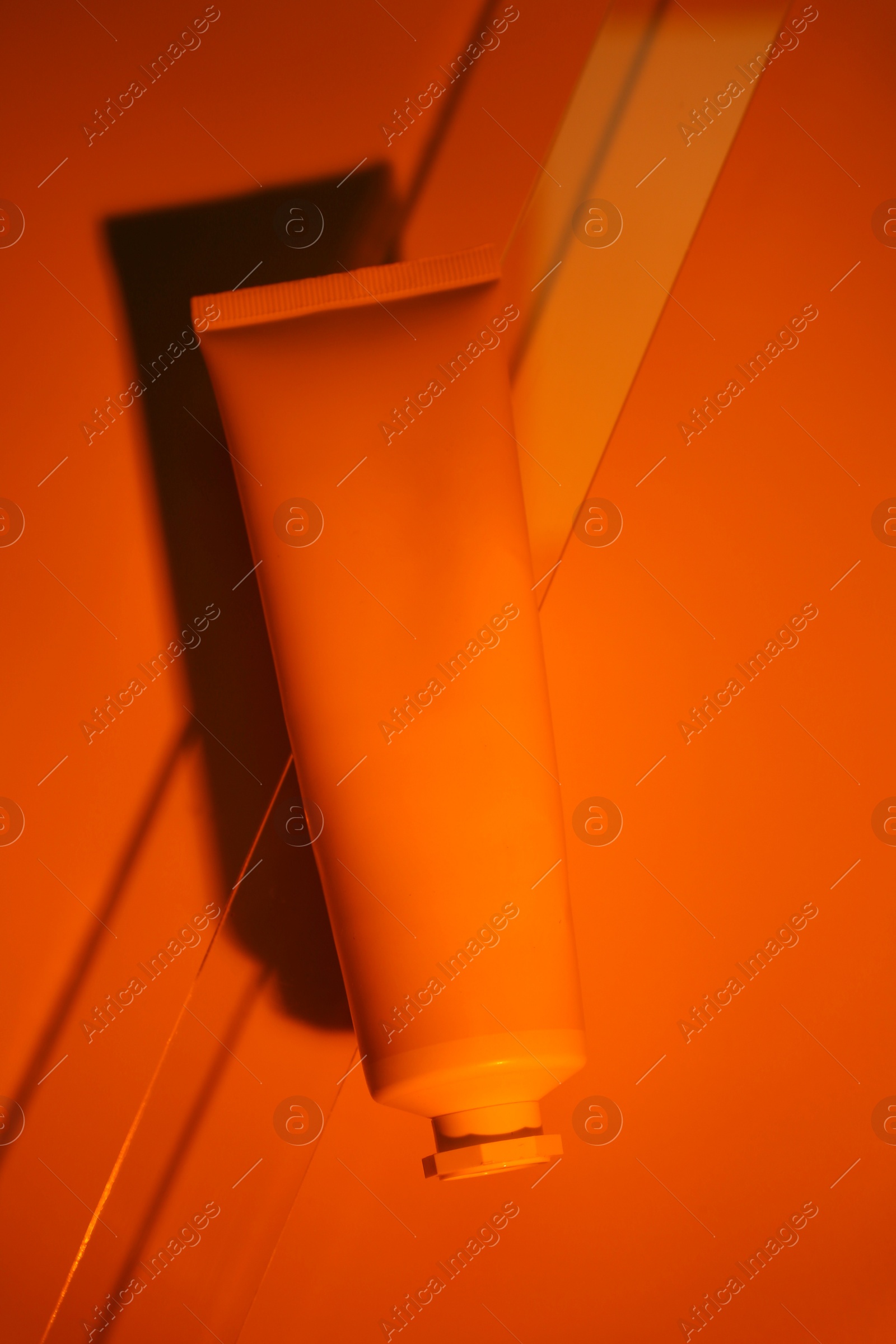 Photo of Tube of cream on dark orange background, top view. Stylish presentation of skincare product