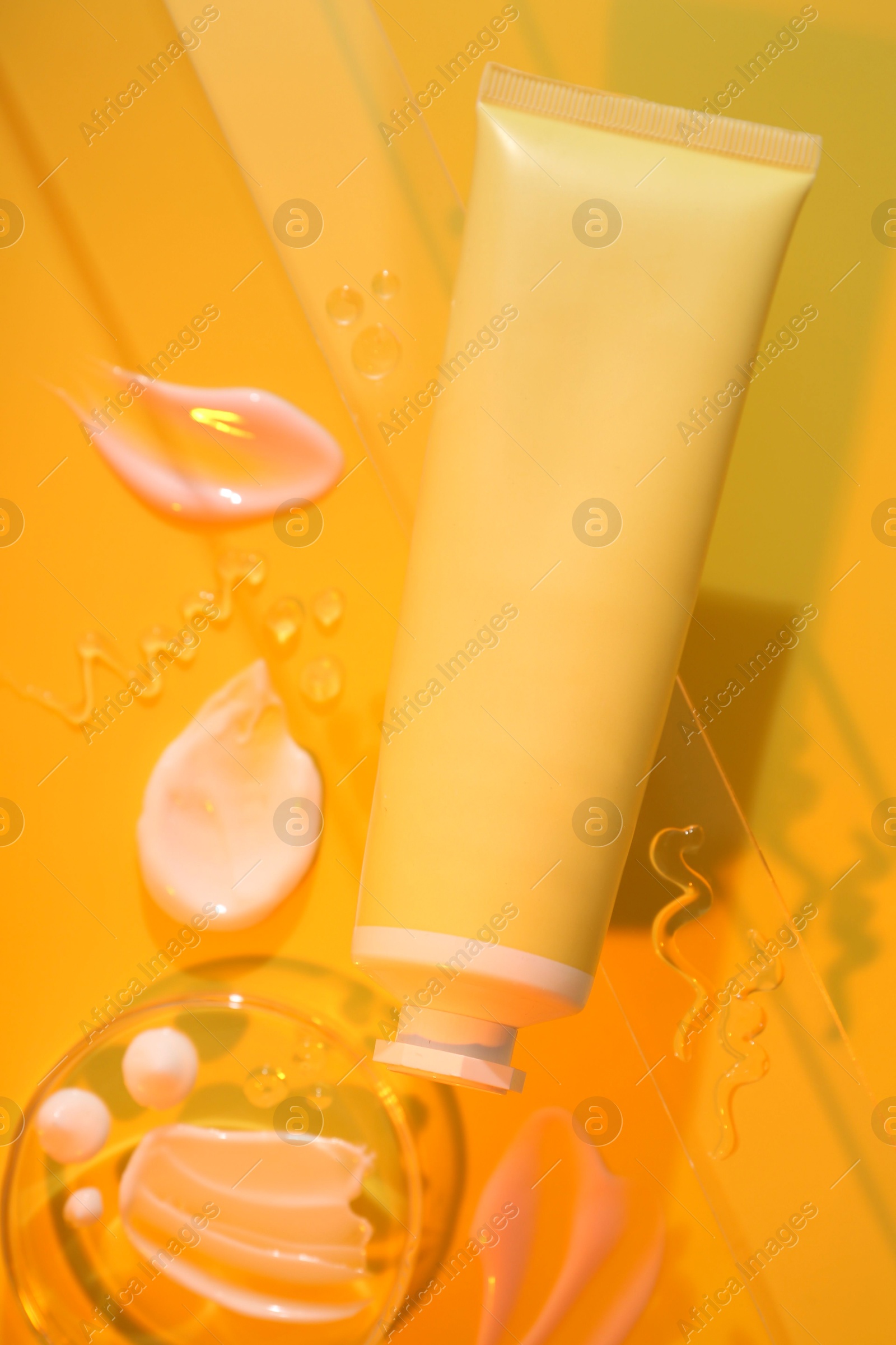 Photo of Cream and gel samples on orange background, flat lay. Stylish presentation with tube of skincare product