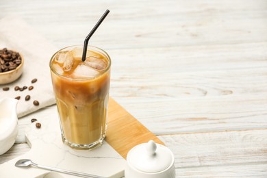 Photo of Refreshing iced coffee with milk in glass and beans on white wooden table. Space for text