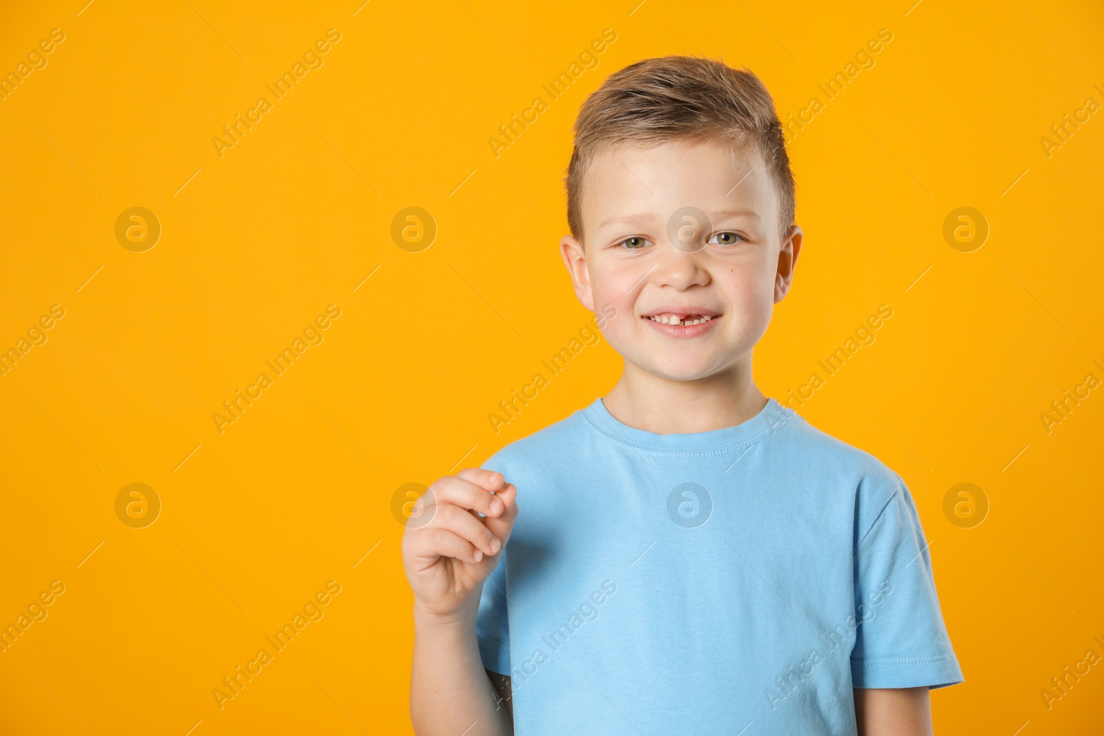 Photo of Cute little boy with missing tooth on orange background, space for text. Waiting for tooth fairy