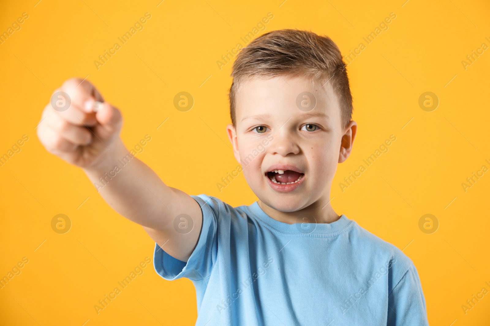 Photo of Cute little boy with missing tooth on orange background. Waiting for tooth fairy