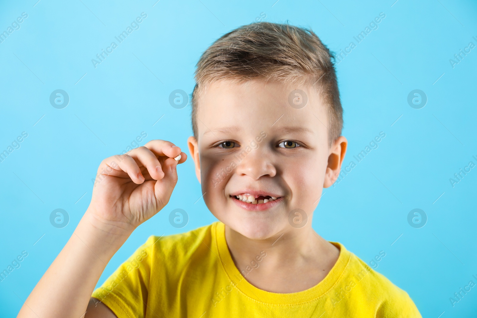 Photo of Cute little boy with missing tooth on light blue background. Waiting for tooth fairy