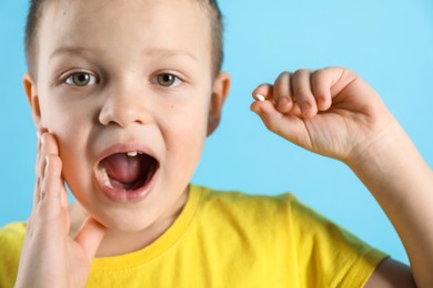 Photo of Cute little boy with missing tooth on light blue background, closeup. Waiting for tooth fairy