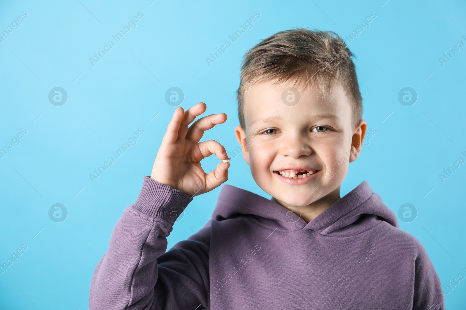 Photo of Cute little boy with missing tooth on light blue background. Waiting for tooth fairy