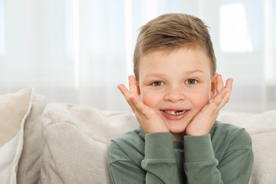 Photo of Cute little boy with missing tooth on sofa at home