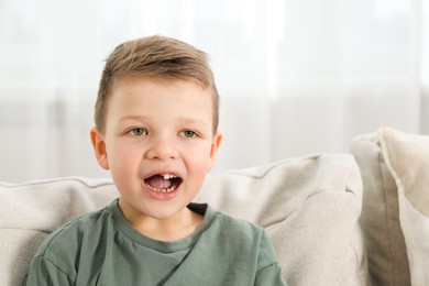 Photo of Cute little boy with missing tooth on sofa at home