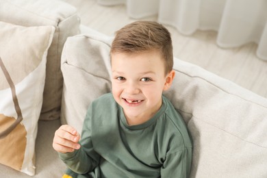 Photo of Cute little boy with missing tooth on sofa at home. Waiting for tooth fairy