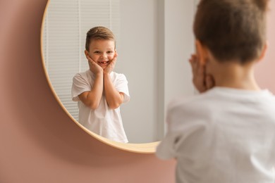 Photo of Cute little boy with missing tooth near mirror indoors