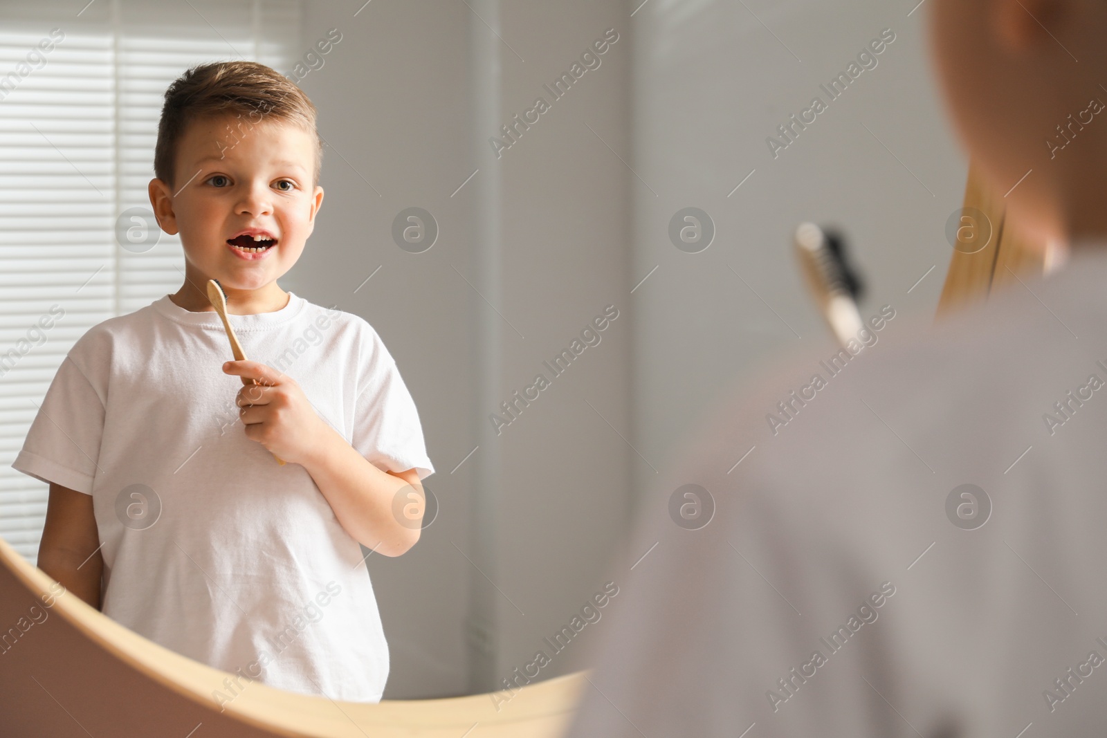 Photo of Cute little boy with missing tooth and toothbrush near mirror indoors