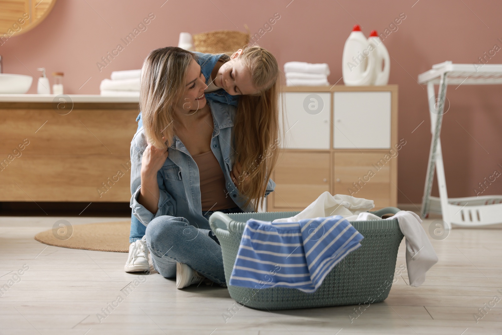 Photo of Little girl and her mom doing laundry together at home