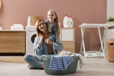 Photo of Little girl and her mom doing laundry together at home