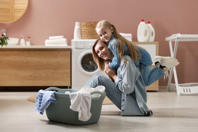 Mother and daughter having fun while doing laundry together at home