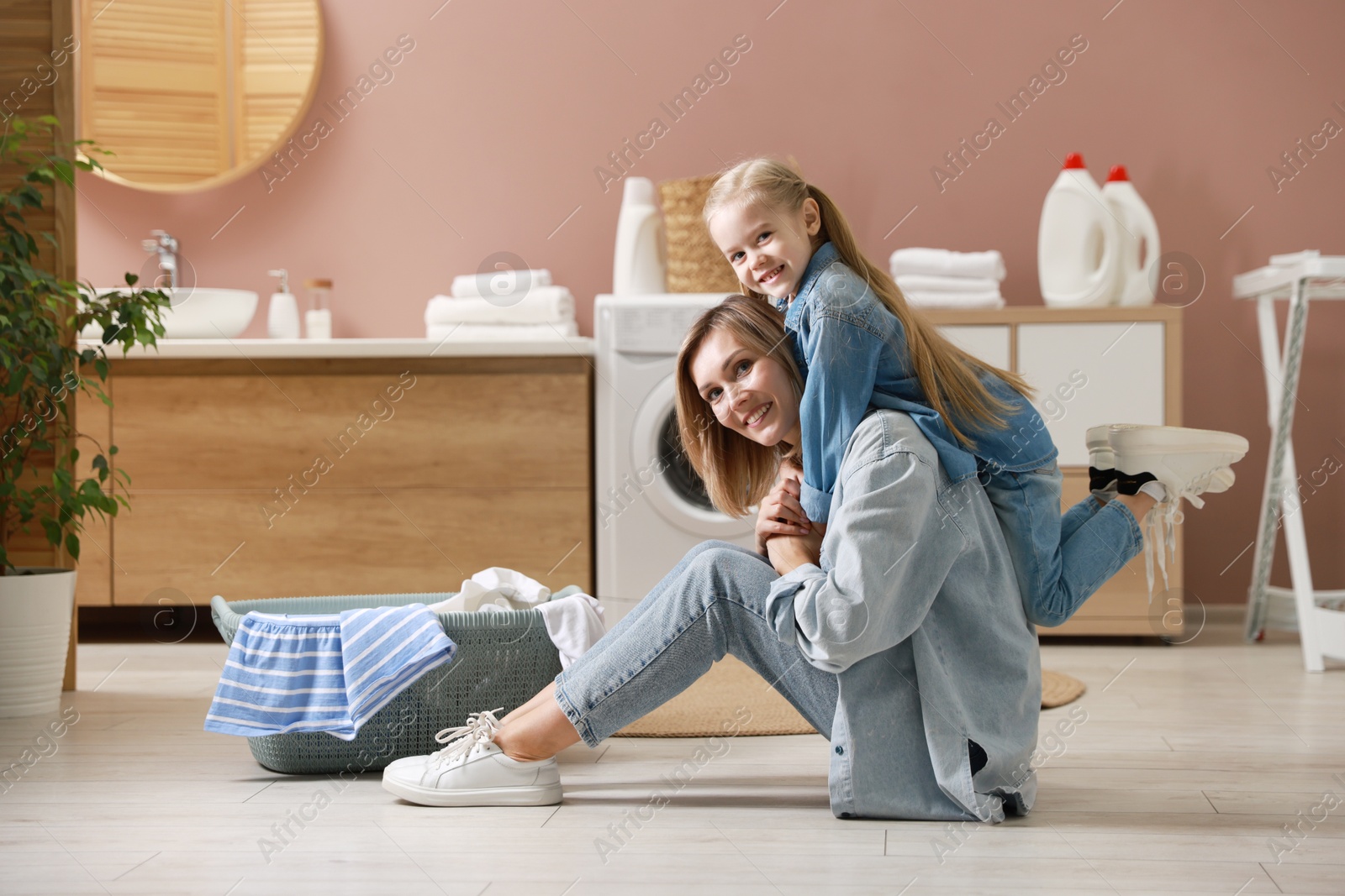 Photo of Mother and daughter having fun while doing laundry together at home