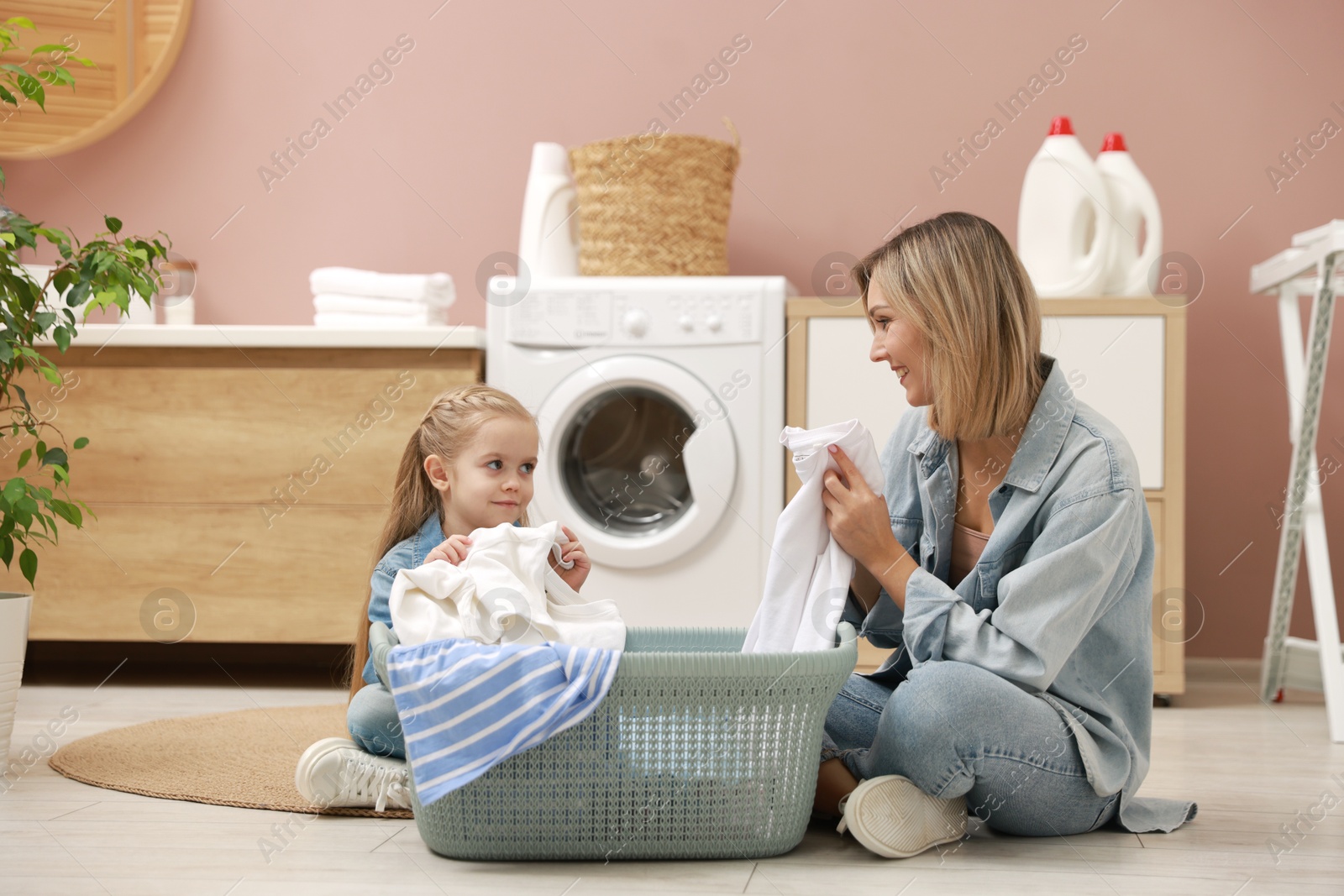 Photo of Little girl and her mom doing laundry together at home