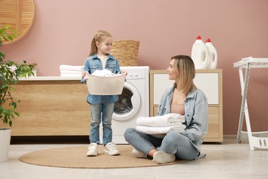 Photo of Little girl and her mom doing laundry together at home