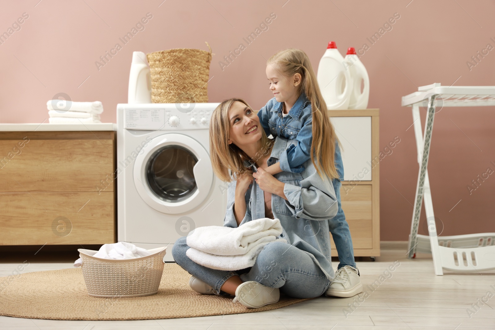 Photo of Little girl and her mom doing laundry together at home