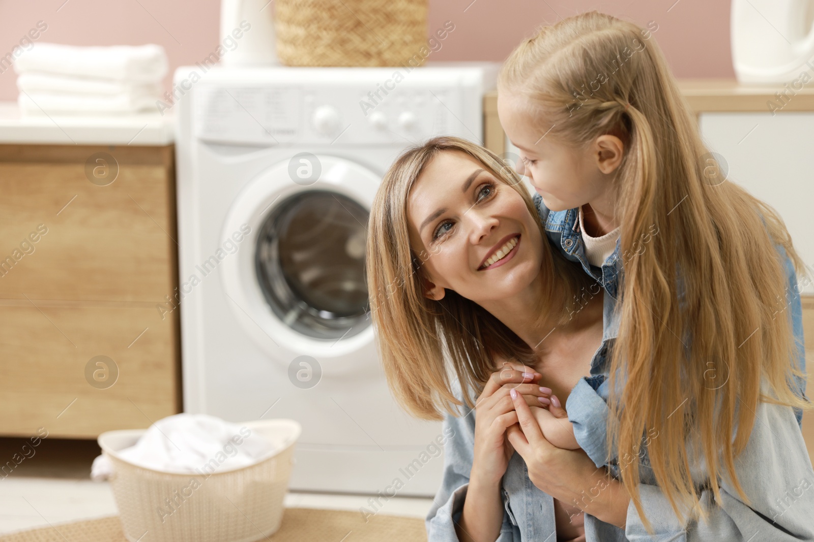 Photo of Little girl and her mom doing laundry together at home