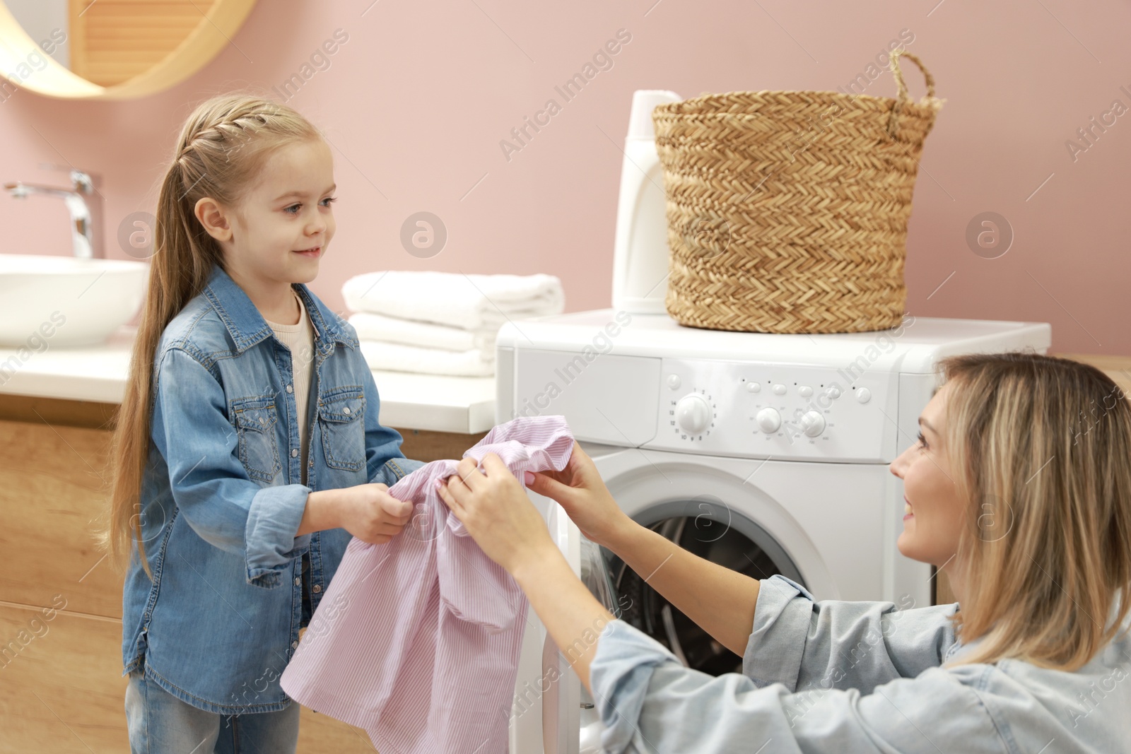 Photo of Mother and daughter loading washing machine together at home