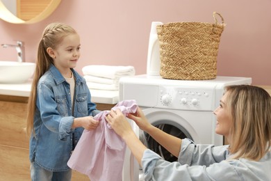 Photo of Mother and daughter loading washing machine together at home