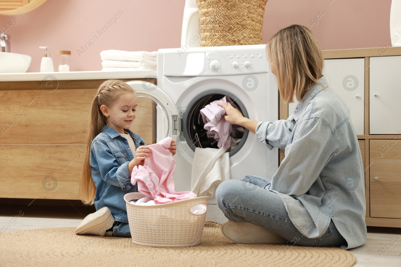 Photo of Mother and daughter with laundry basket loading washing machine together at home