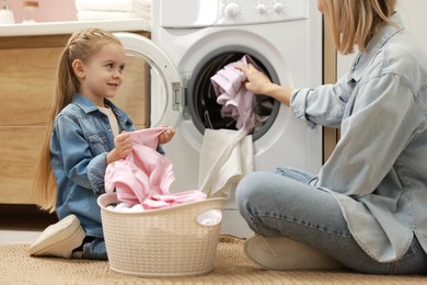 Mother and daughter with laundry basket loading washing machine together at home