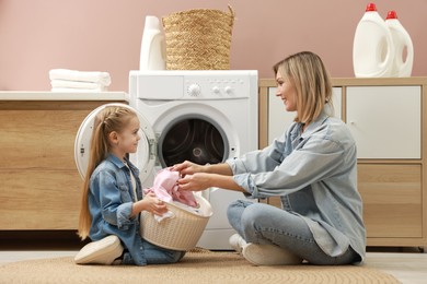 Photo of Mother and daughter with laundry basket loading washing machine together at home