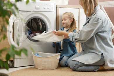 Photo of Mother and daughter with laundry basket loading washing machine together at home