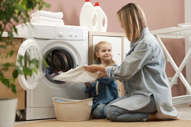 Photo of Mother and daughter with laundry basket loading washing machine together at home