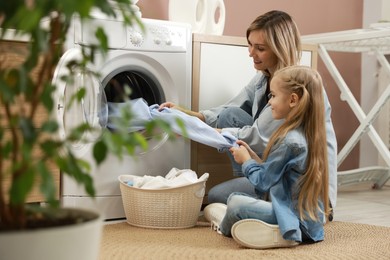 Photo of Mother and daughter with laundry basket loading washing machine together at home