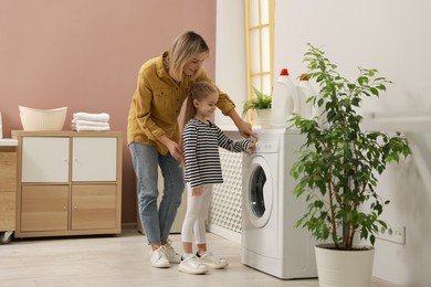 Photo of Little girl and her mom doing laundry together at home