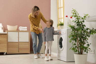 Photo of Little girl and her mom doing laundry together at home