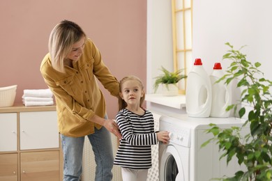 Photo of Little girl and her mom doing laundry together at home