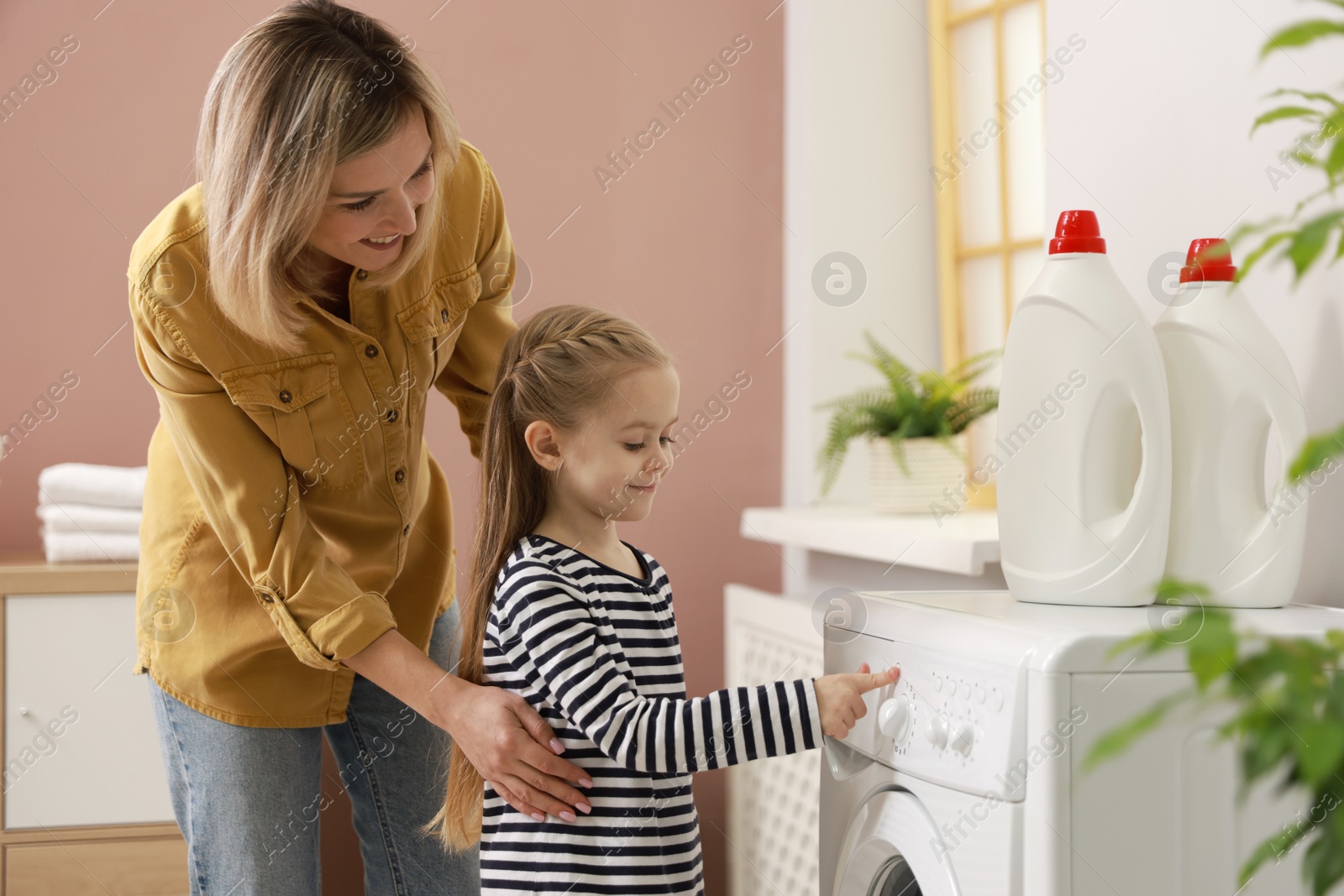 Photo of Little girl and her mom doing laundry together at home