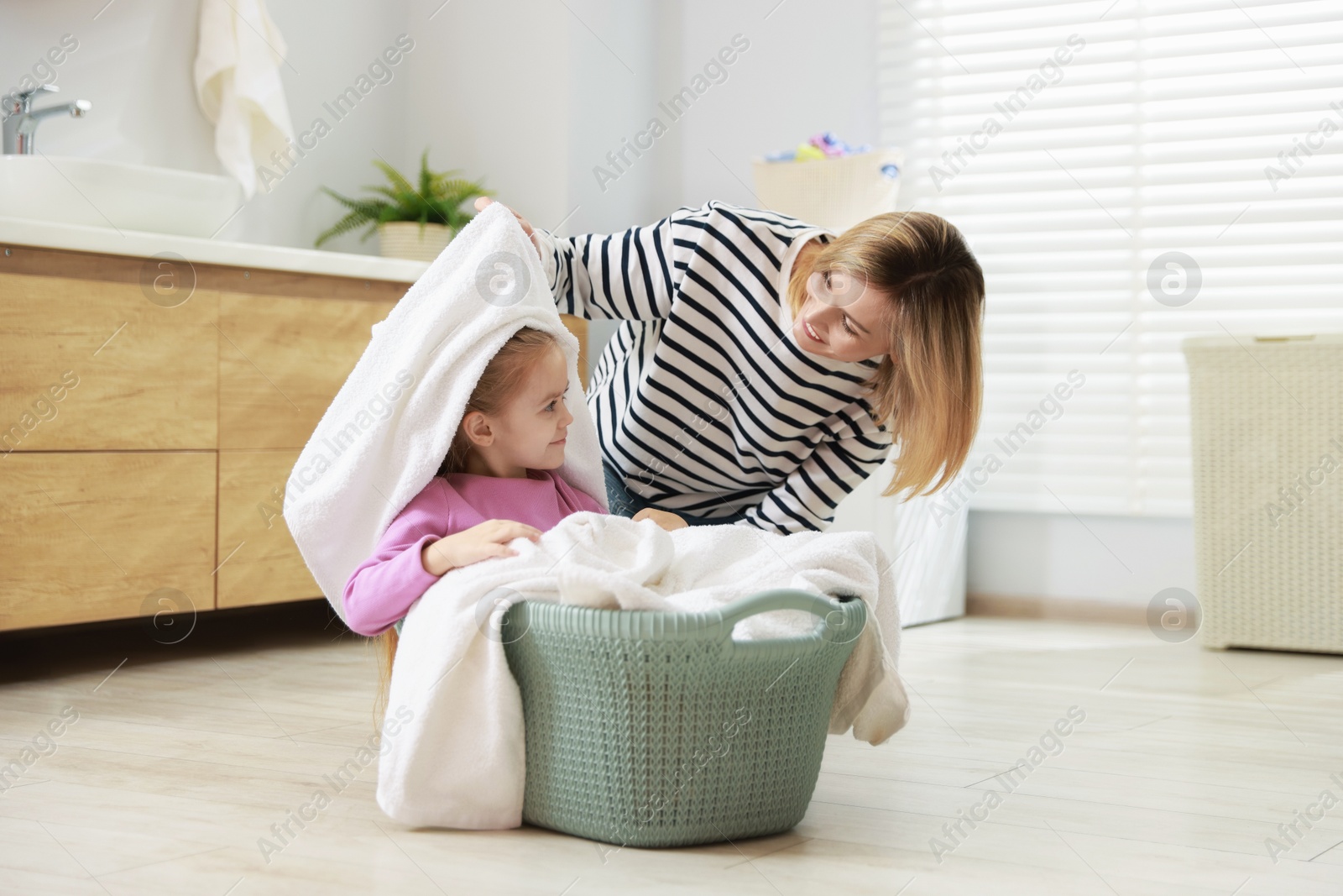 Photo of Little girl and her mom doing laundry together at home