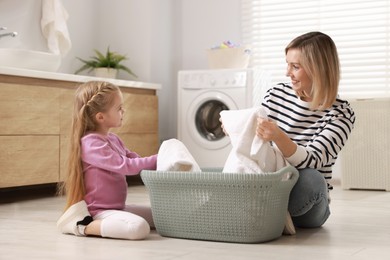 Photo of Little girl and her mom doing laundry together at home