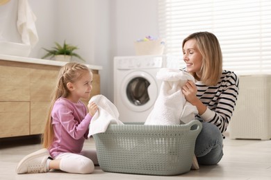 Photo of Little girl and her mom doing laundry together at home