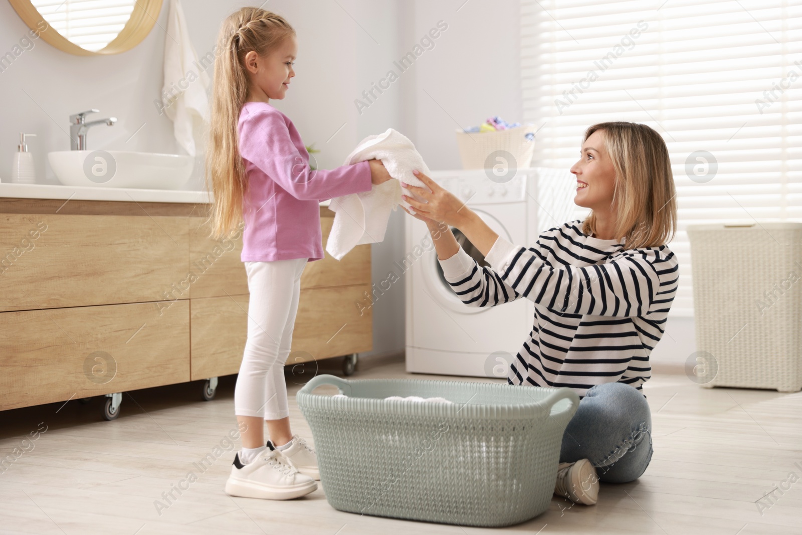 Photo of Little girl and her mom doing laundry together at home