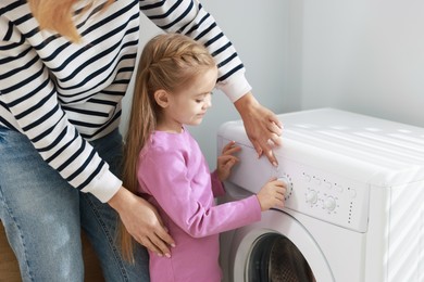 Photo of Little girl and her mom doing laundry together at home