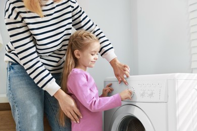 Photo of Little girl and her mom doing laundry together at home