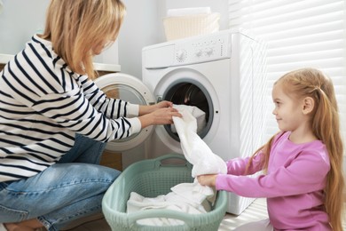 Photo of Mother and daughter with laundry basket loading washing machine together at home