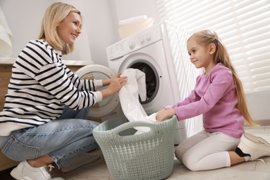 Photo of Mother and daughter with laundry basket loading washing machine together at home