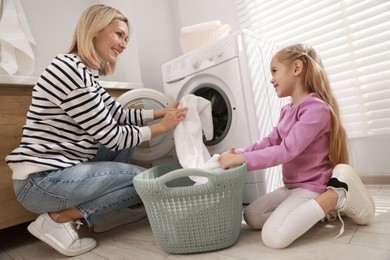 Photo of Mother and daughter with laundry basket loading washing machine together at home