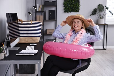 Photo of Businesswoman with inflatable ring, flower wreath, bag and straw hat at workplace in office