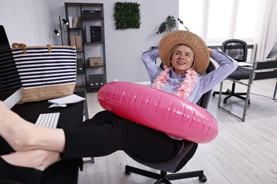 Businesswoman with inflatable ring, flower wreath, bag and straw hat at workplace in office